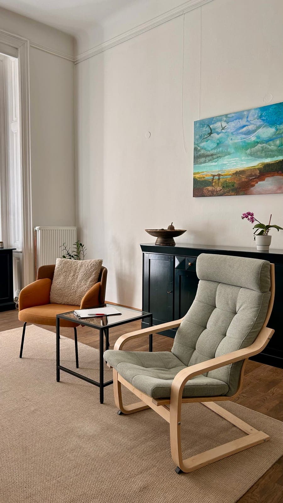 Two armchairs facing each other across a low table, with a painting and a sideboard behind them