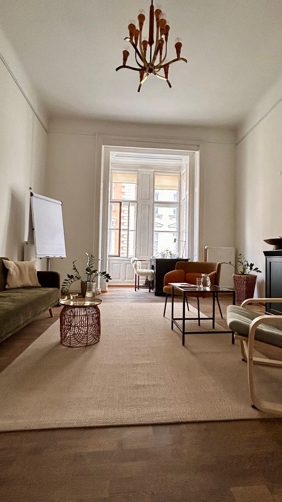 The practice room: a sofa, two armchairs and a small table under a chandelier, with a tall window at the far end